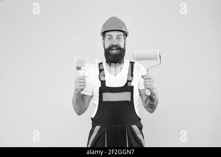 Felice pittore in abiti da lavoro tenere rullo di vernice e spazzolatura strumenti di pittura per lavori di costruzione e di costruzione, finitura. Foto Stock