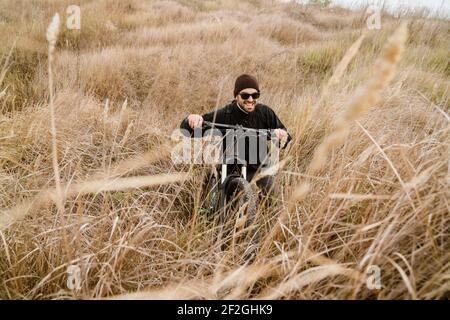 Stanco unshaven ragazzo in occhiali da sole che cammina con la sua bicicletta campo Foto Stock