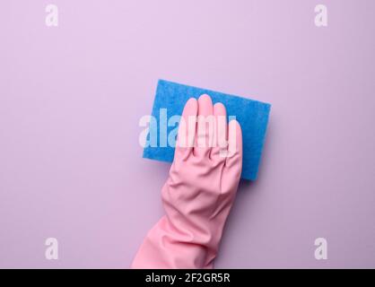 la mano femminile in guanto di gomma rosa tiene la spugna blu da cucina su sfondo viola, primo piano Foto Stock