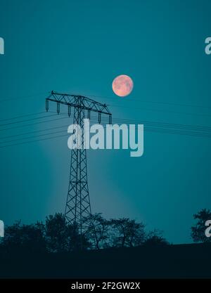 La luna nel cielo notturno sullo sfondo di linee elettriche Foto Stock