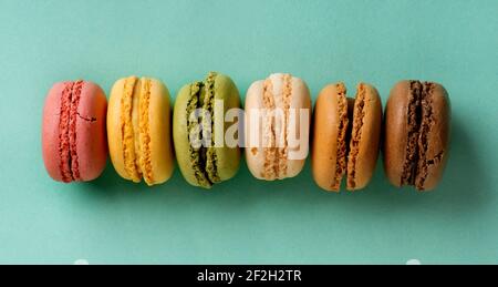 Dolce macarons colorati in una fila su un sfondo turchese Foto Stock