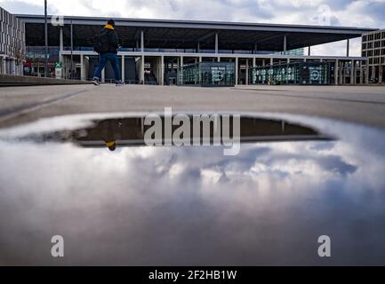 12 marzo 2021, Brandeburgo, Schönefeld: Terminal 1 dell'aeroporto della capitale Berlino il Brandeburgo "Willy Brandt" (BER) si riflette in una pozza. Nel pomeriggio si svolge una riunione del Consiglio di sorveglianza della Flughafen Berlin-Brandenburg GmbH. L'argomento principale è le future esigenze finanziarie dell'azienda. La società di gestione conta sulla riduzione parziale del debito da parte degli stati di Berlino, Brandeburgo e governo federale. Foto: Patrick Pleul/dpa-Zentralbild/ZB Foto Stock