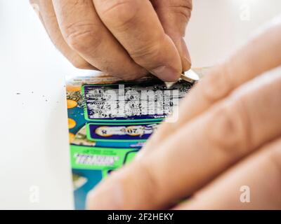 Primo piano POV senior mano maschile graffiare con moneta d'oro Cash biglietto di graffiatura istantanea della lotteria con numeri fortunati Foto Stock