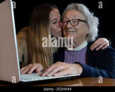 Giovane nipote che dà un abbraccio e baciare la vecchia donna degli anni 80 nonna mentre sta insegnando ad usare il laptop a casa.spese della famiglia tempo e divertimento insieme Foto Stock