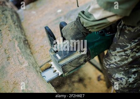 Uomo in camouflage sega di legno spessa motosega. Polvere volante dalla bevanda Foto Stock