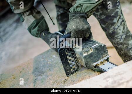 Uomo in camouflage sega di legno spessa motosega. Polvere volante dalla bevanda Foto Stock