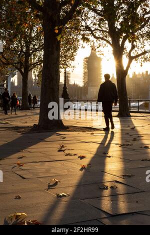 Pedoni che camminano oltre il Tamigi in luce dorata tardo pomeriggio, con il Palazzo di Westminster sullo sfondo, South Bank, Londra Foto Stock