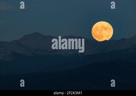 Idilliaco scatto di luna piena sulla catena montuosa contro chiaro cielo al crepuscolo Foto Stock