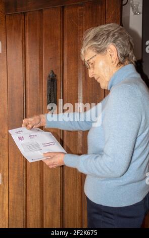 Inghilterra, Regno Unito. 2021. Anziana donna alla sua porta d'ingresso apre documentaion relativo al censimento britannico che ogni residente di Inghilterra e Galles deve comple Foto Stock