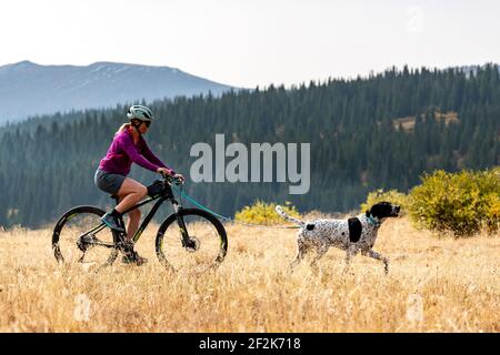 Vista laterale di una donna sorridente in bicicletta dietro il cane sul campo durante le vacanze Foto Stock