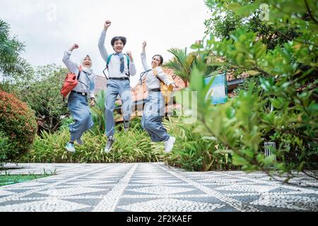 Tre studenti indonesiani delle scuole superiori hanno saltato nelle loro borse scolastiche alzando le mani insieme Foto Stock