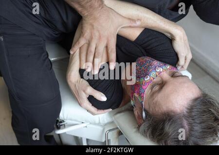 La donna con la maschera facciale che giace sulla barella ottiene la regolazione del corpo dell'osteopata. Fisioterapista anonimo premendo sul petto della paziente femminile, fisioterapista Foto Stock