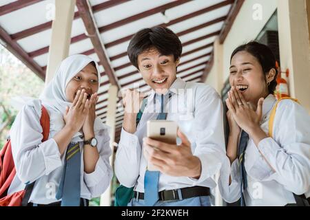 un primo piano di tre studenti delle scuole superiori esamina il schermo utilizzando uno smartphone per vedere l'annuncio della laurea Foto Stock