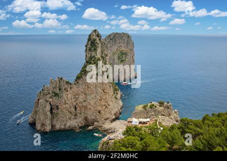 Vista su un ristorante e una spiaggia rocciosa tra le scogliere di Faraglioni. Vista sulle famose rocce dei Faraglioni nel blu del Tirreno, isola di Capri, Italia Foto Stock