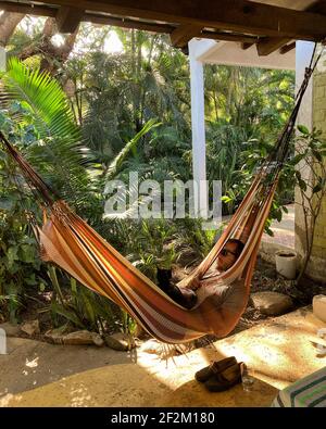 Un uomo allatta un gatto mentre riposa in un'amaca ad un Airbnb a Sayulita, Messico Foto Stock