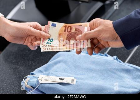 Il cliente maschile consegna banconote € al registratore di cassa di un negozio di moda, donna di vendita in un negozio di tessili, solo le mani visibili Foto Stock