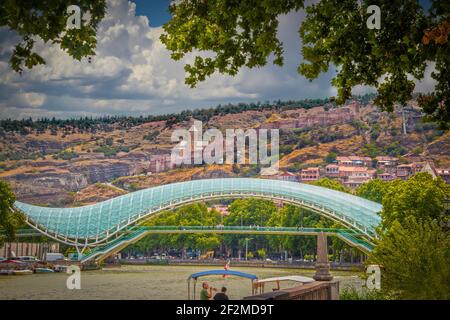 2019 07 19 Tbilisi Georgia - Ponte della Pace con l'antica fortezza di Narikala Si affaccia su Tbilisi e si affaccia sulle rive del fiume Mtkvari - Kura con barca Foto Stock