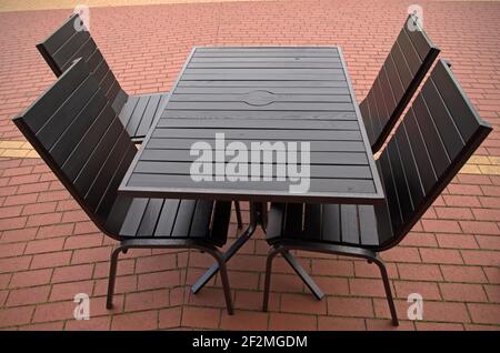 Tavolo nero in legno e quattro sedie nere con gambe in metallo sulla terrazza estiva patio di accogliente caffetteria sul rosso con strisce gialle pavimento piastrellato del pa Foto Stock