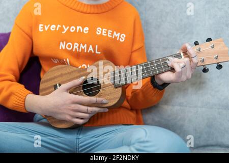 primo piano delle mani di una giovane donna irriconoscibile in sneakers che suonano l'ukulele al tramonto in città, concetto di musica amatoriale e li artistici Foto Stock