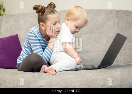 Bambina e ragazzo carino che usano il computer portatile insieme, guardando lo schermo, guardando i cartoni animati o giocando online, sorella e fratello, fratelli seduti su comfor Foto Stock