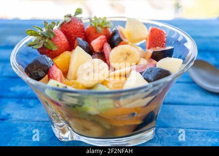 Insalata di frutta naturale e sana con arancia in un recipiente di vetro trasparente, su una superficie rustica - blu. Concetto di cibo sano, vita sana. 45 gradi Foto Stock