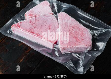 Filetto di tonno crudo congelato in set sottovuoto, su vecchio sfondo di tavola di legno scuro Foto Stock