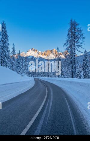 Valle Fiorentina, strada attraverso la foresta innevata, sullo sfondo le Dolomiti baciate dal sole. Passo Staulanza, Selva di cadore, belluno, veneto, italia Foto Stock