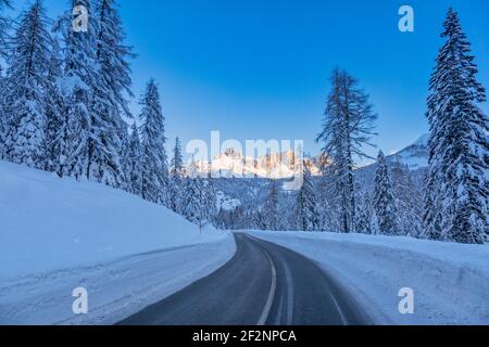 Valle Fiorentina, strada attraverso la foresta innevata, sullo sfondo le Dolomiti baciate dal sole. Passo Staulanza, Selva di cadore, belluno, veneto, italia Foto Stock