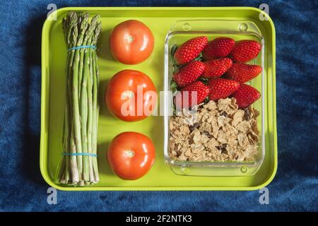 Una muffa di vetro riempita con fragole, grani interi e cioccolato fondente su un vassoio con pomodori e asparagi selvatici. Alimentazione sana. Foto Stock