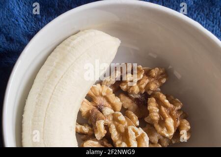 Una manciata di noci e mezza banana sbucciata su un piatto. Spuntini sani, frutta e noci. Foto Stock