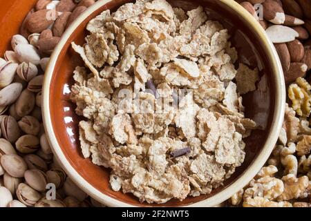 Vista dall'alto di un mucchio di riso tostato, grano intero e fiocchi d'orzo con scaglie di cioccolato con diverse noci secche sullo sfondo. Foto Stock