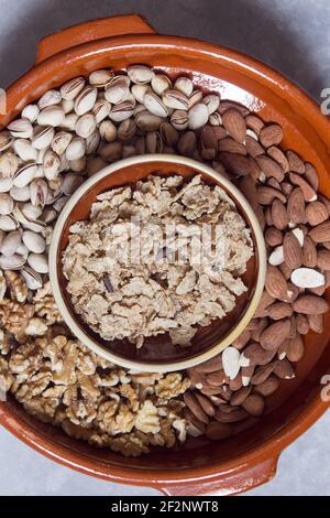 Una vecchia pentola di terracotta riempita con frutta secca mista con una ciotola di argilla riempita con cereali e trucioli di cioccolato su uno sfondo di pietra testurizzata. Foto Stock