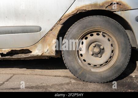 Corrosione della lamiera sulla ruota della vecchia auto bianca. Superficie arrugginita e disordinata. Grana sporca danneggiata dal sale della strada. Sfondo ruggine. Protezione di Foto Stock