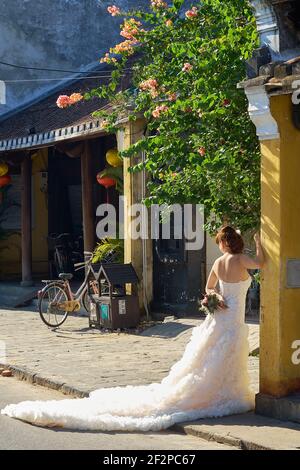 Foto urbana della sposa vietnamita in un elegante abito da sposa bianco nelle colorate strade della città vecchia di Hoi An in Vietnam Foto Stock