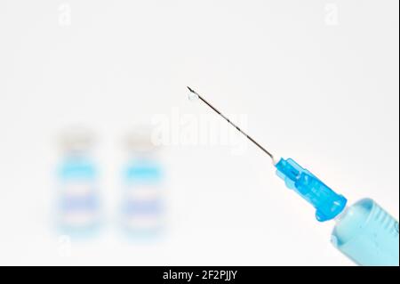 Concetto medico - primo piano della siringa con ago contenente liquido blu. Sfondo offuscato con flaconcini per vaccino COVID-19. Isolato su sfondo bianco Foto Stock