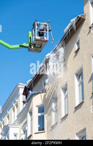 Germania, Sassonia-Anhalt, Magdeburgo, un uomo colpisce le iciclette con una pala dalla grondaia di un edificio di appartamenti. Foto Stock