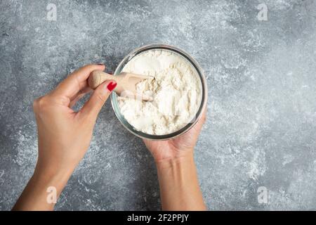 Donna che tiene il cucchiaio all'interno del recipiente della farina Foto Stock