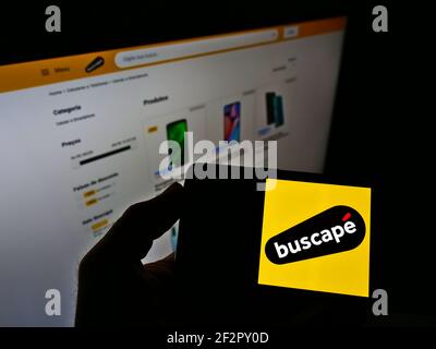 Persona che tiene smartphone con il logo del negozio online brasiliano Buscapé sullo schermo di fronte al sito web. Mettere a fuoco il display del telefono. Foto non modificata. Foto Stock