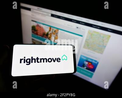 Persona che tiene smartphone con logo del portale online del settore immobiliare britannico Rightmove plc sullo schermo di fronte al sito web. Mettere a fuoco il display del telefono. Foto Stock