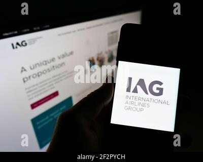 Persona che detiene un telefono cellulare con il logo della compagnia aerea International Airlines Group (IAG) sullo schermo davanti alla pagina web. Mettere a fuoco il display del telefono. Foto Stock