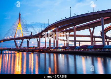 Pittoresca vista sottostante dello svincolo autostradale e dei ponti sospesi al tramonto. Le luci si riflettono sul fiume. Thailandia. Foto Stock