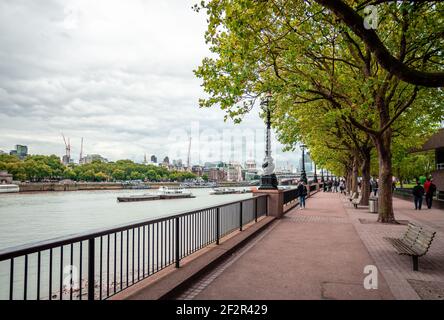 Londra, UK - Aprile 22 2014: La Queen's Walk in South Bank, vicino al fiume Tamigi. Lo skyline della città di Londra è sullo sfondo. Foto Stock