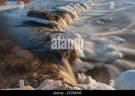 un'ampia cascata d'inverno con ghiaccio e neve si fonde in una lunga esposizione creando una sensazione di relax guardando il flusso d'acqua Foto Stock