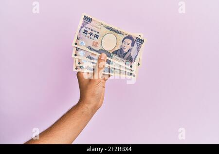 Mano ispanica che tiene 5000 yen giapponesi su sfondo rosa isolato. Foto Stock