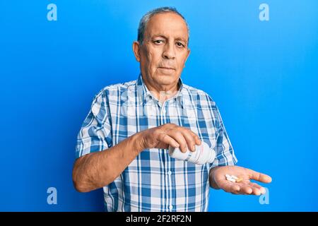 L'uomo ispanico anziano che tiene le pillole rilassato con l'espressione seria sul viso. Semplice e naturale guardare la macchina fotografica. Foto Stock