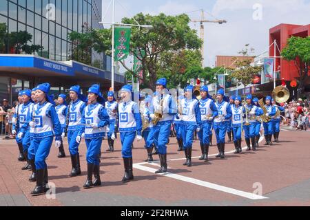 I membri di Falun Dafa (Falun Gong), una religione cinese, marciando lungo la strada con abiti tradizionali blu e bianchi che suonano strumenti musicali Foto Stock