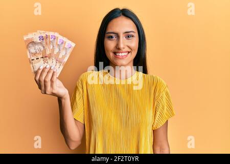 Giovane donna bruna che tiene in Sud africa 20 rand banconote cercando positivo e felice in piedi e sorridente con un sorriso fiducioso mostrare i denti Foto Stock