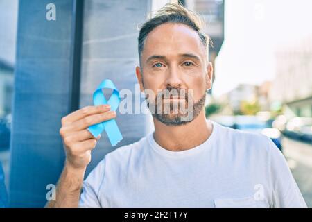 Bell'uomo di mezza età con espressione seria che tiene il nastro blu del cancro della prostata alla città. Foto Stock