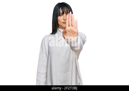 Giovane donna bruna con pangs che indossa un pullover casual turtleneck facendo smettere di cantare con il palmo della mano. Avvertimento espressione con negativo e serio Foto Stock