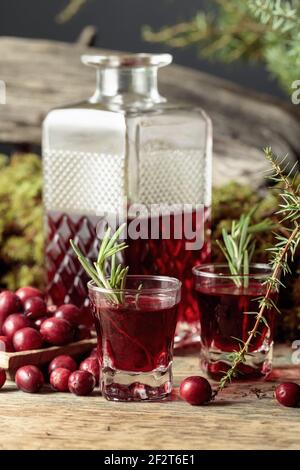 Mirtilli rossi e liquori di mirtilli su un vecchio tavolo di legno. Nello sfondo muschio, ramo di ginepro, e vecchio snag. Foto Stock